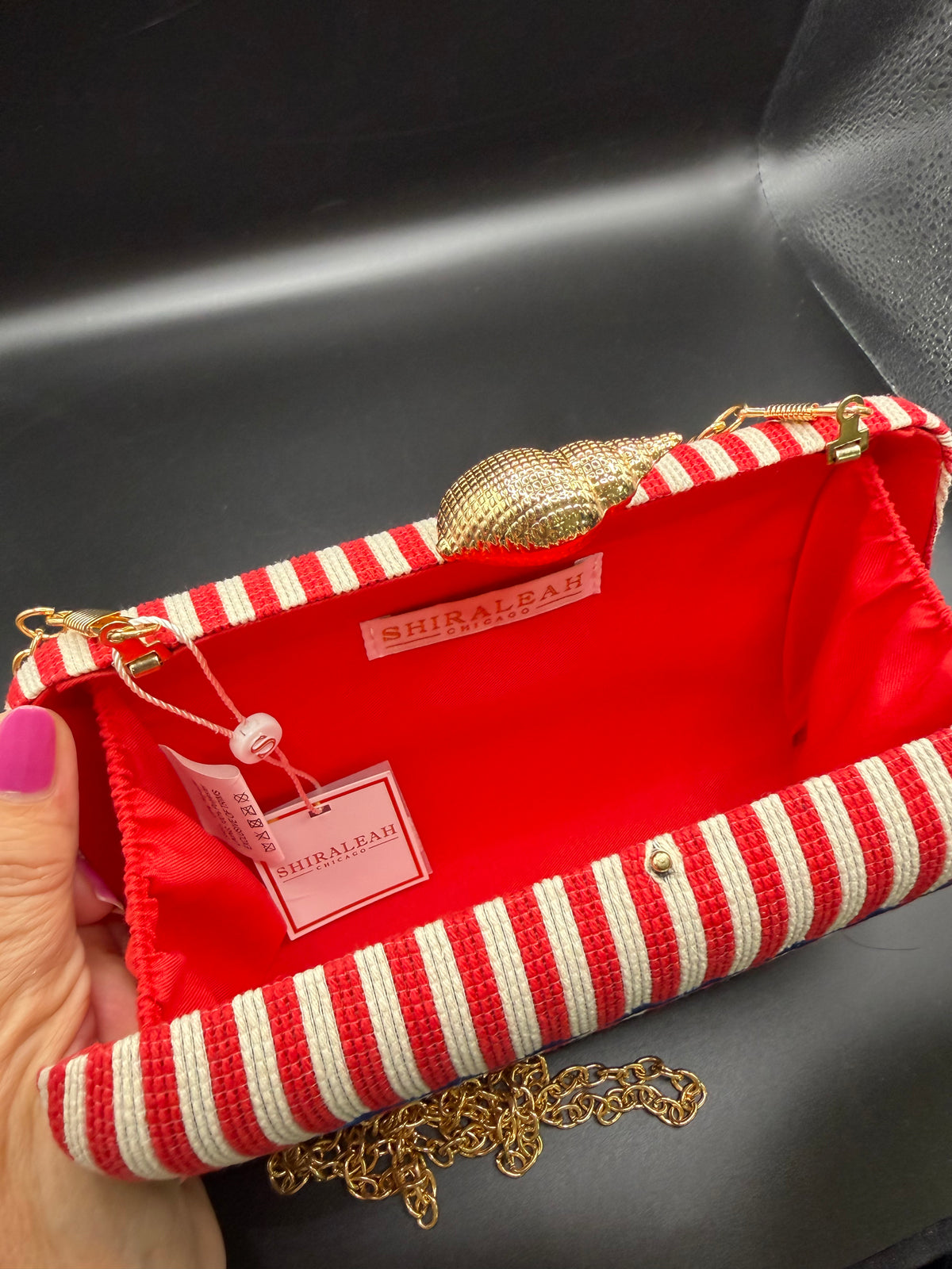 The selected item is the Shiraleah Marina Red Striped Lobster Minaudière Clutch.This nautical-inspired evening bag features a structured box silhouette dressed in bold red and white vertical stripes. It is accented by a prominent, bright blue embroidered