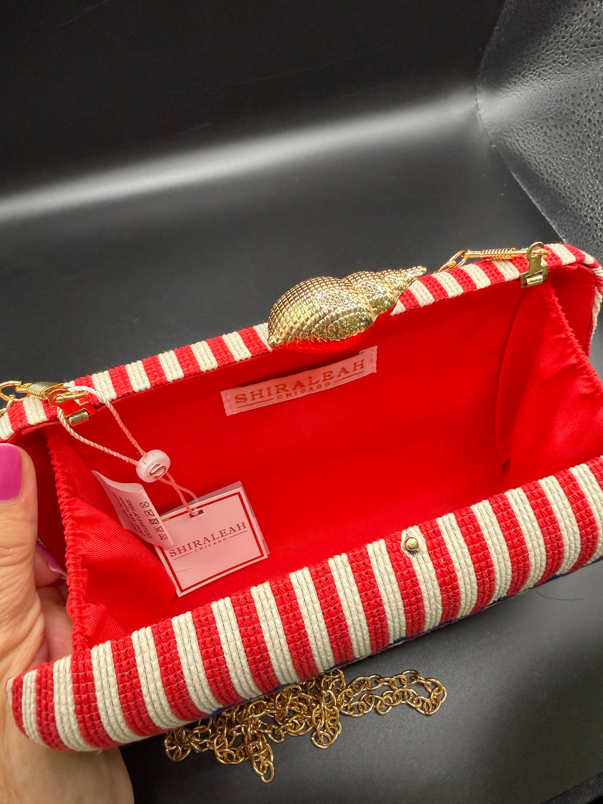 The selected item is the Shiraleah Marina Red Striped Lobster Minaudière Clutch.This nautical-inspired evening bag features a structured box silhouette dressed in bold red and white vertical stripes. It is accented by a prominent, bright blue embroidered